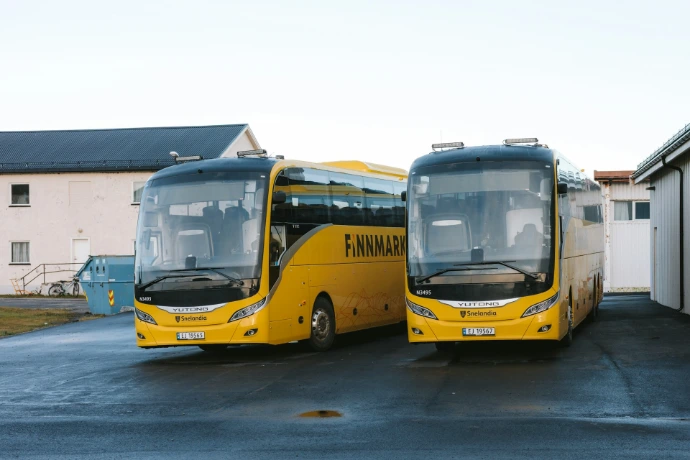 Two yellow tour buses parked outside buildings